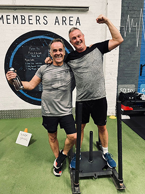 Two men celebrating next to a weighted sled in the members' area