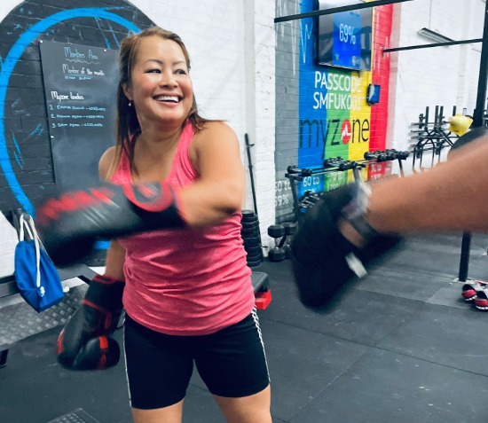 Smiling woman in boxing gloves punching pads during a class
