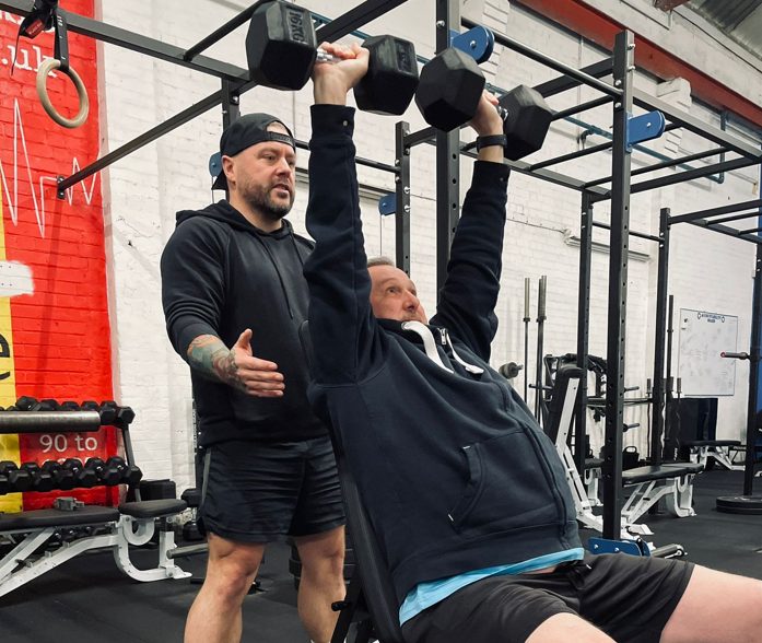 Personal trainer coaching a member through an incline dumbbell press