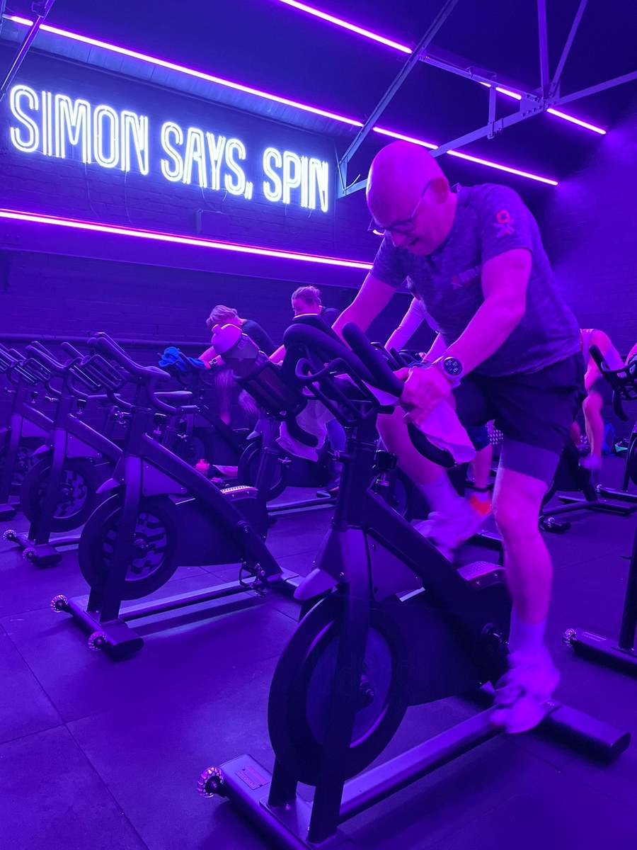 Member riding a spin bike under purple lights in the Simon Says Spin class