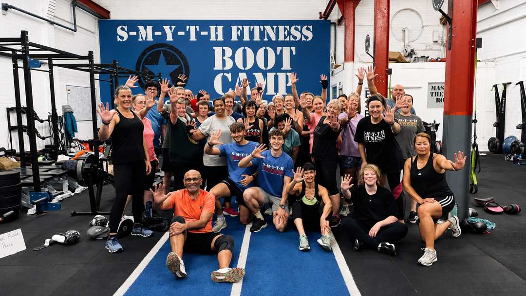 Large group of Smyth Fitness members cheering together in front of the Boot Camp wall