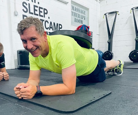 Smiling man holding a weighted plank on a gym mat